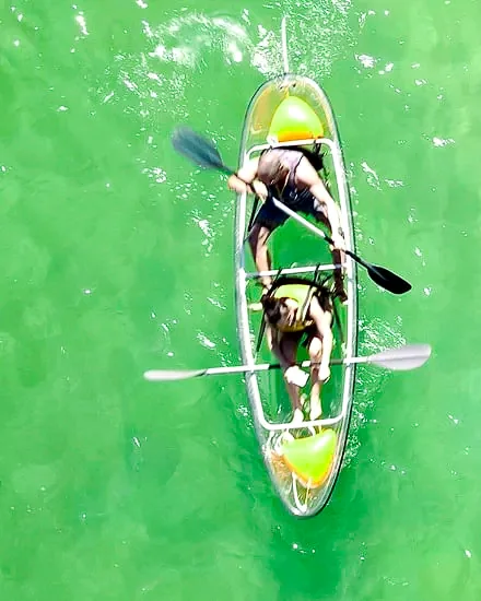 Two people sharing a clear double kayak on green shallows