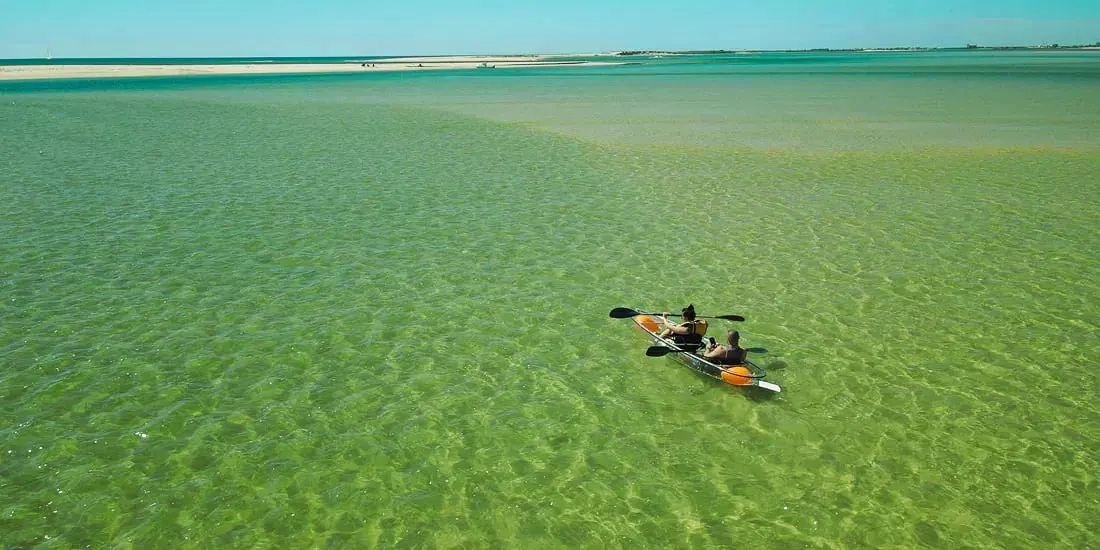 A clear kayak crossing rippled shallow water, from high above