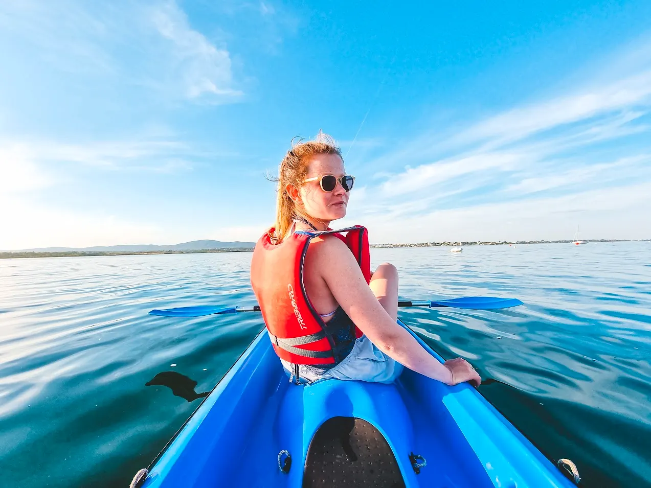 A paddler in a red life jacket in a blue kayak on calm water